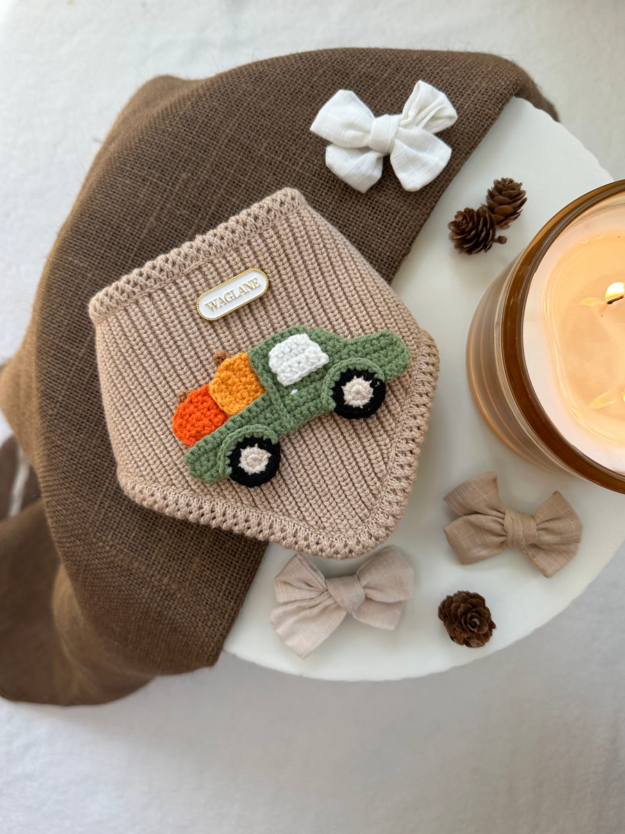 Knitted dog  bandana with crochet applique, surrounded by small bows and a candle on a textured round surface.