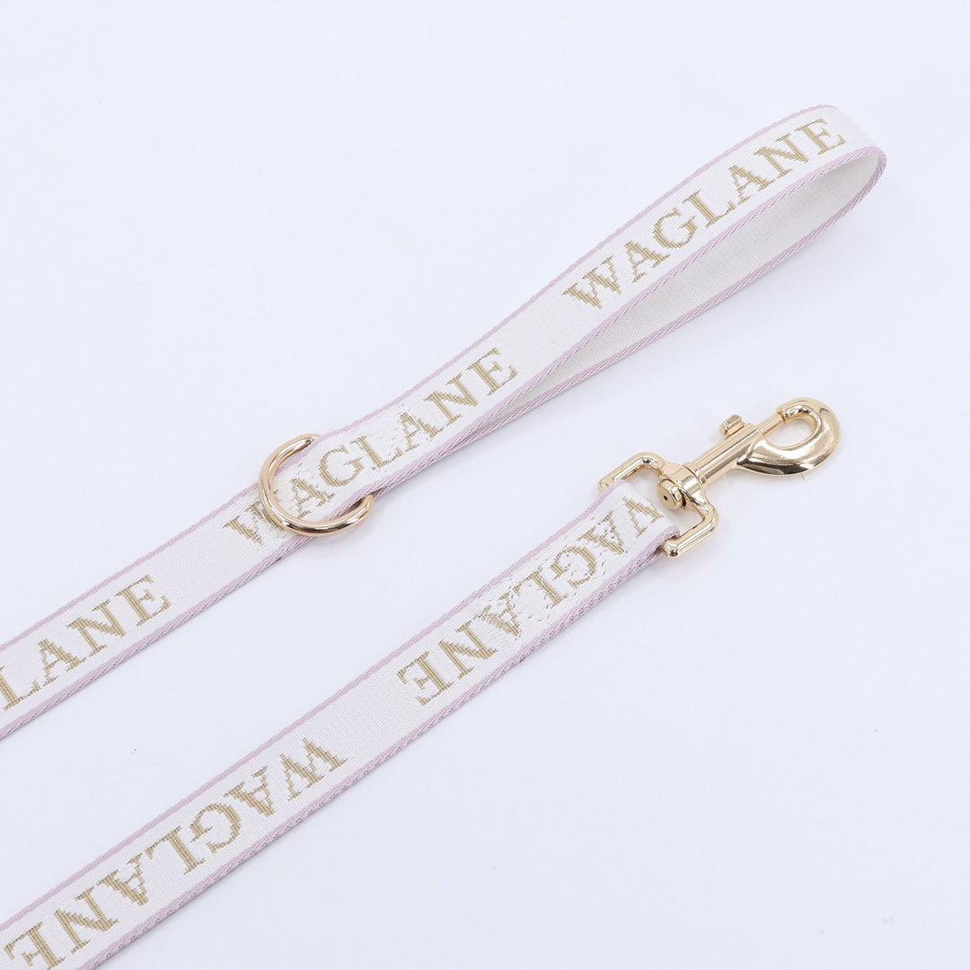 Flat lay blush creme webbing leash with tan jacquard 'WAGLANE' branding and aesthetic gold hardware