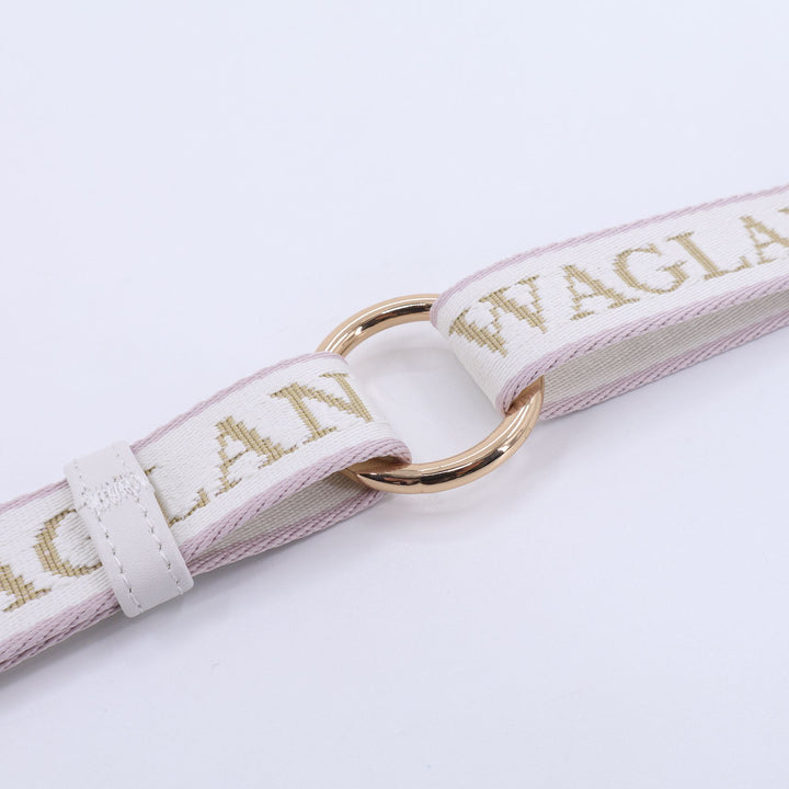 Close-up of a luxury dog leash featuring ivory and blush woven strap with gold or brown “WAGLANE” lettering, connected by a polished gold metal ring and white leather size adjuster detailing.